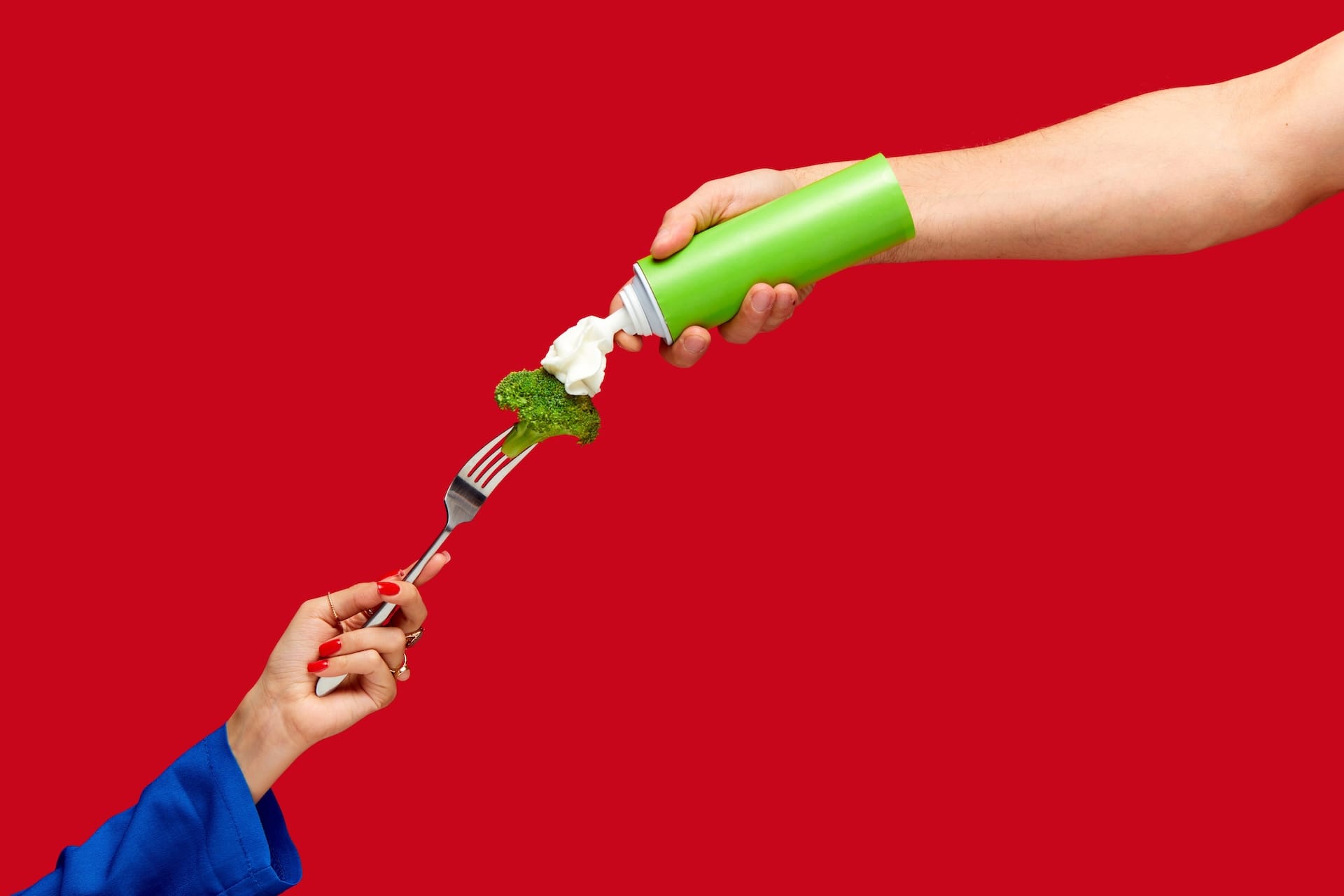 Hand reaching out to squirt some cream on a piece of broccoli