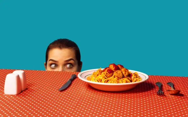 Woman hiding behind a bowl of spaghetti